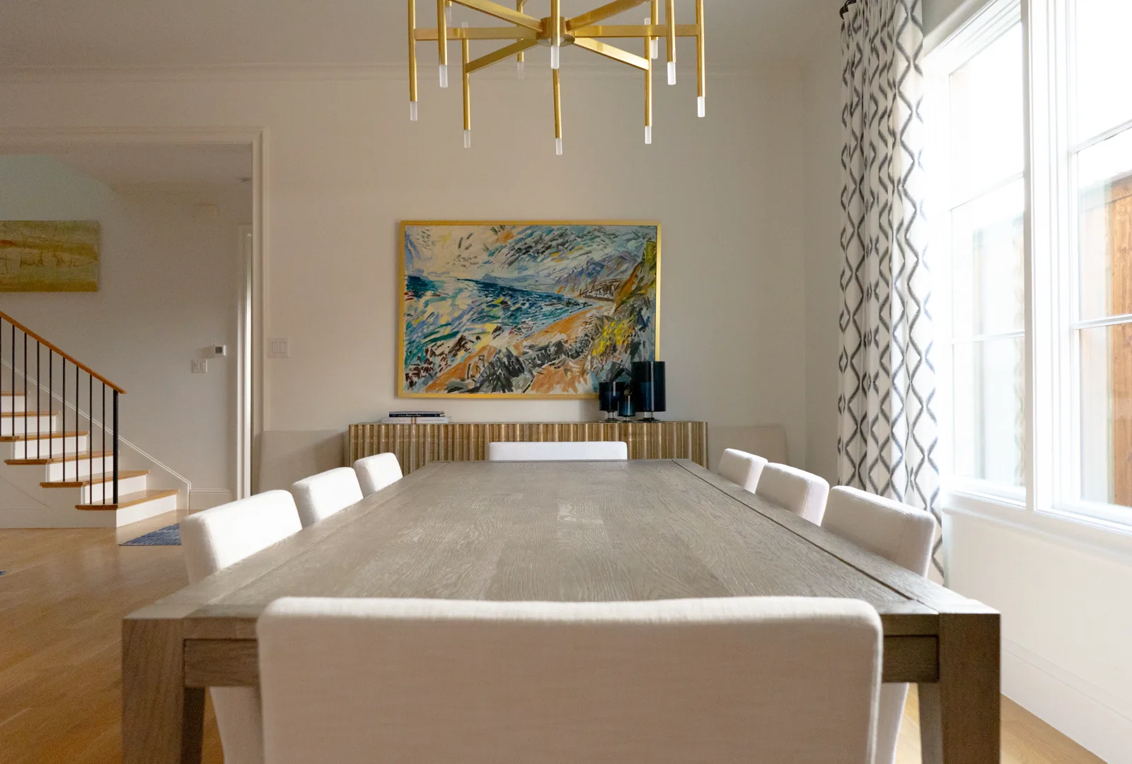 Dining room by The Look by Lina with a pale oak table, brass chandelier, and colorful artwork