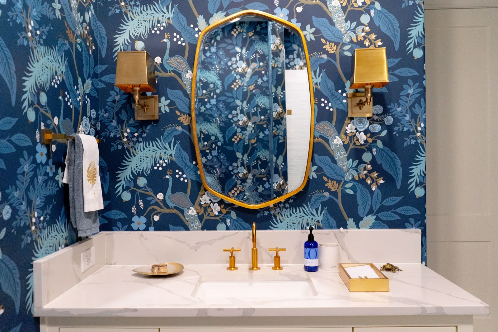 Deep blue botanical powder room with a brass mirror and sconces
